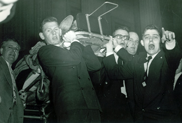 In this image taken moments after the shooting, (from left foreground) House Pages Bill Goodwin, Paul Kanjorski, and Bill Emerson carry a stretcher bearing a wounded Member to a waiting ambulance. Photo from the Office of the Clerk.